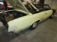 Cream-colored classic car with black rear end, hood and trunk open, in a garage.