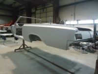 Partially assembled, light gray convertible car body inside a garage.