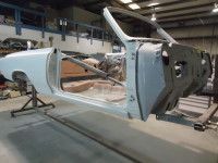 Partially assembled white car chassis in a workshop, supported by stands.