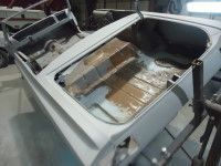 Partially disassembled car trunk, showing rusted floor and interior components in a garage.