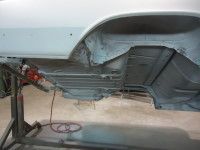 Underside of a car body being worked on, supported by a metal stand, in a workshop.