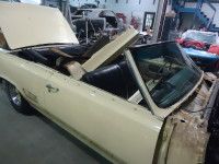 Cream-colored convertible car in a garage with hood up, undergoing restoration.