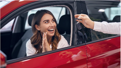 A woman is sitting in a red car while a man gives her a car key.