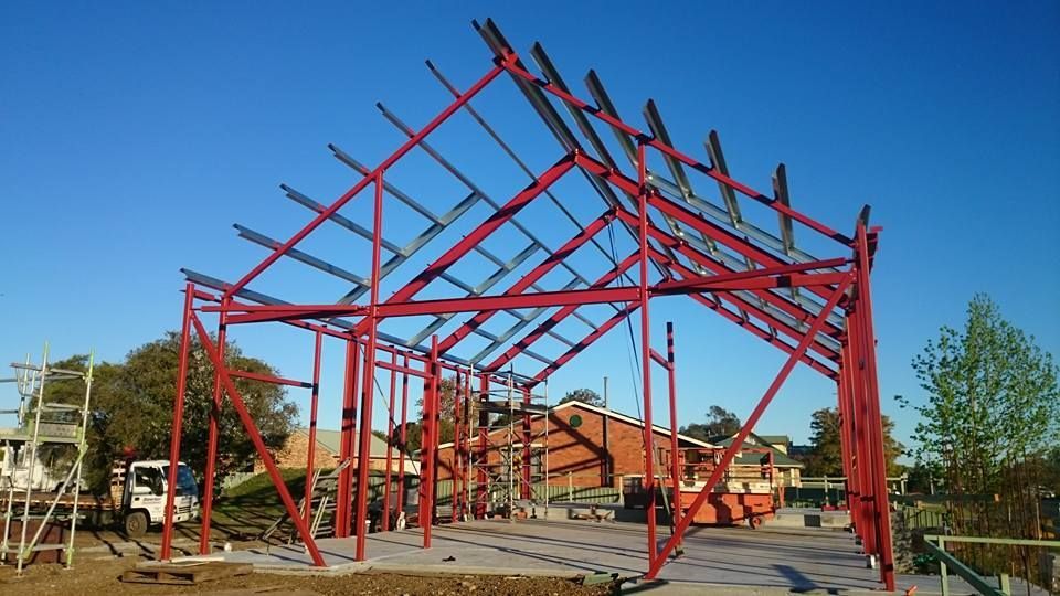 A red large steel frame structure is being built on a construction site — Burke Metal Fabrication In Taree, NSW