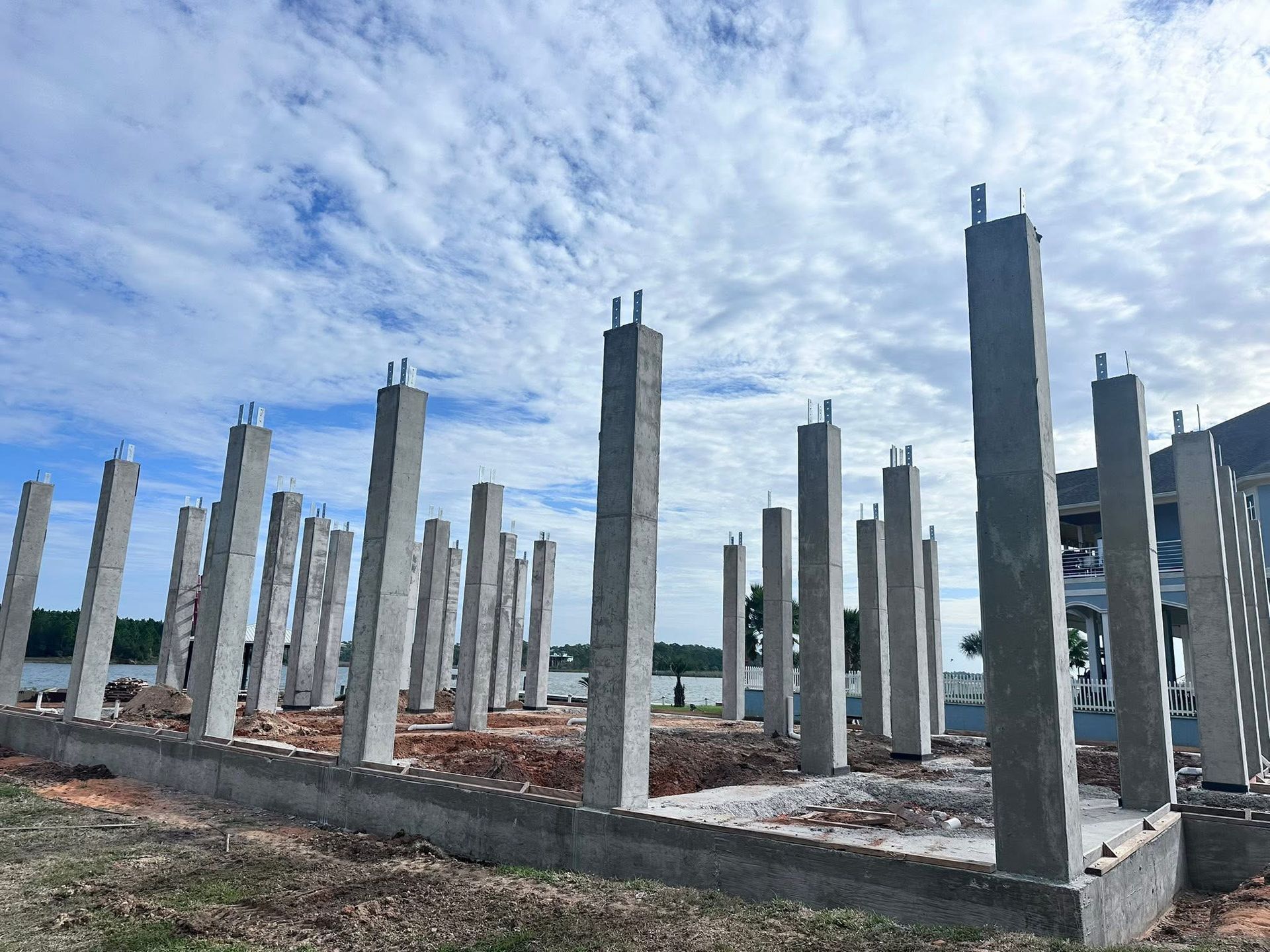 Construction site with concrete support columns under a cloudy blue sky.
