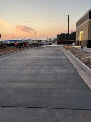 Empty paved road at sunset beside a building and parked cars, with power lines overhead.