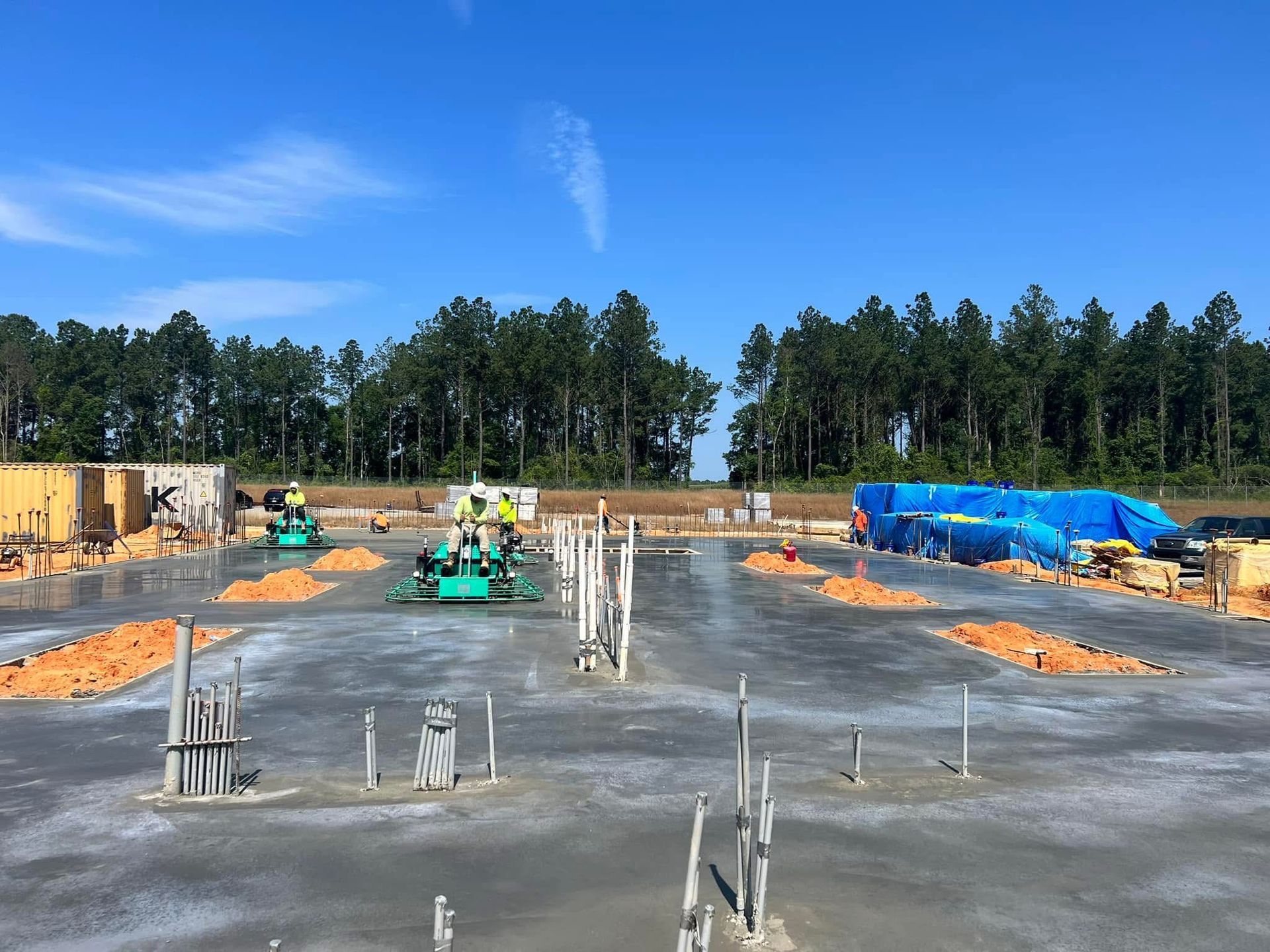 Construction site with concrete slab, workers, equipment, and blue tarps under a clear sky