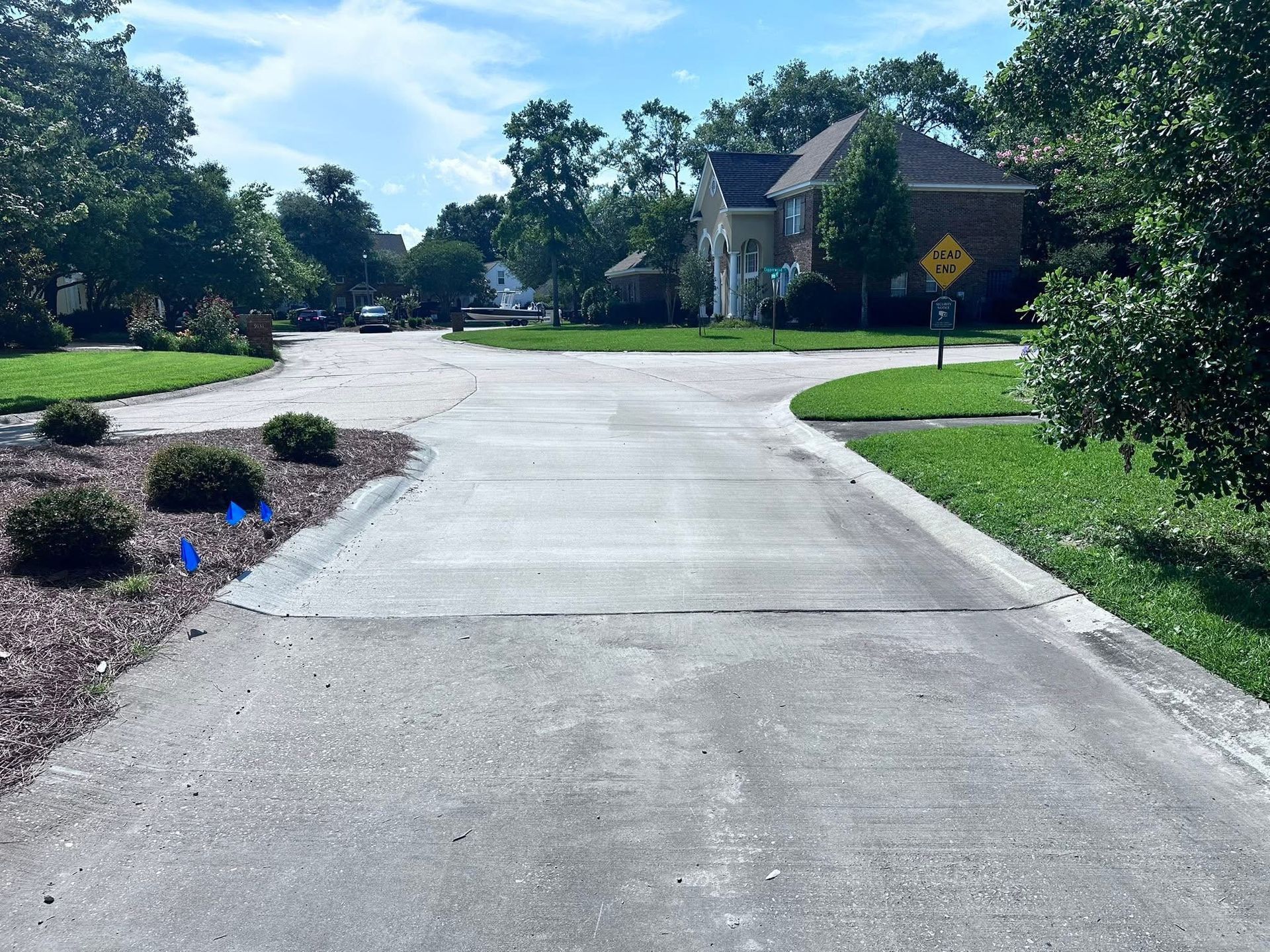 Quiet suburban street with a curved concrete road, grassy lawns, trees, and a brick house on the right