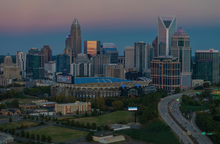 Aerial view of the Charlotte, North Carolina skyline at dusk, featuring Bank of America Stadium in the foreground.