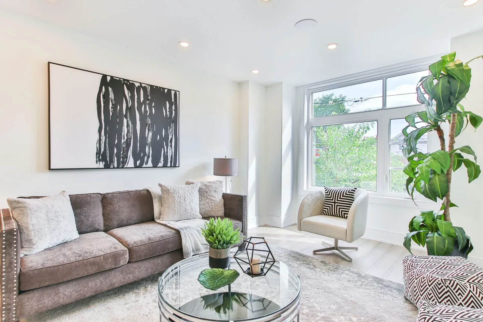 Bright modern living room with a sofa, abstract wall art, large window, and potted plant