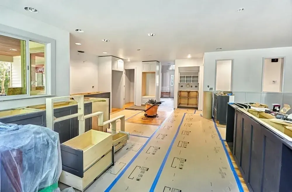 Bright kitchen under renovation with cabinets, counters, and covered floor in a long open room