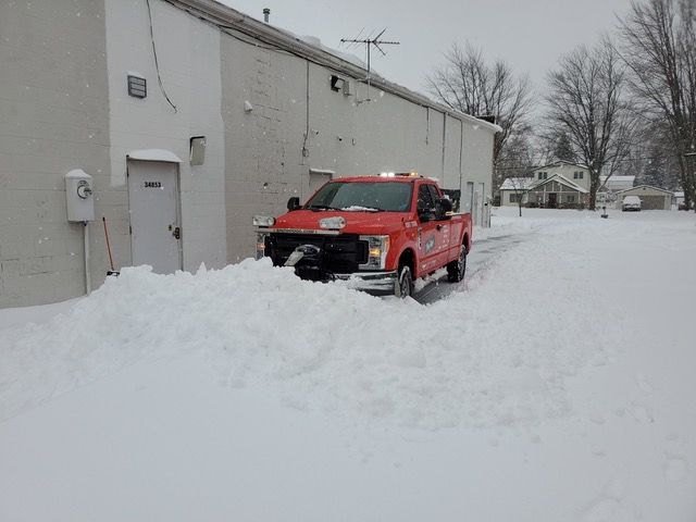 A snow plow is driving down a snowy street next to a dump truck.