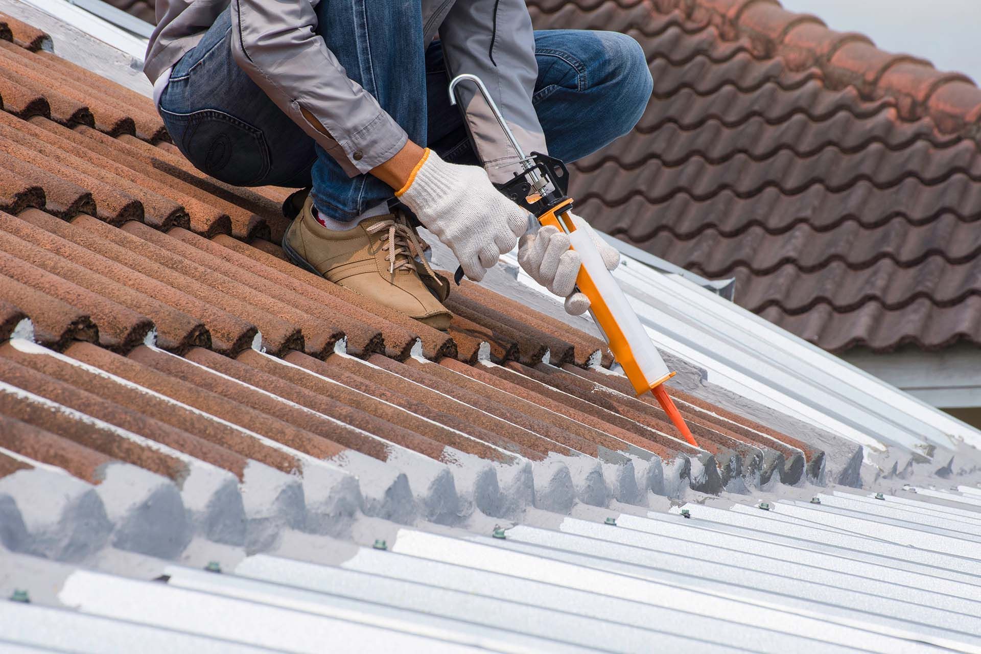A cropped view of a roofer using a glue gun with adhesive or polyurethane to seal a roof.