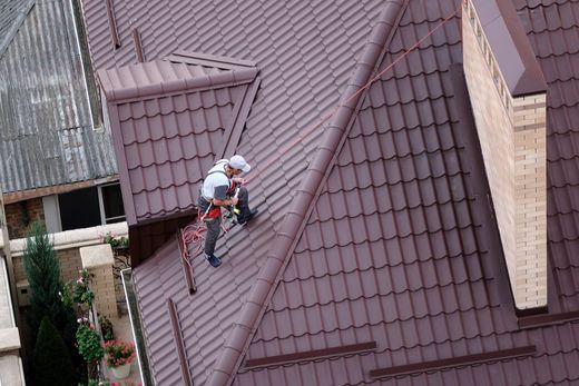 Worker repairing a steep brown roof with a safety harness Worker repairing a steep brown roof with a safety harness