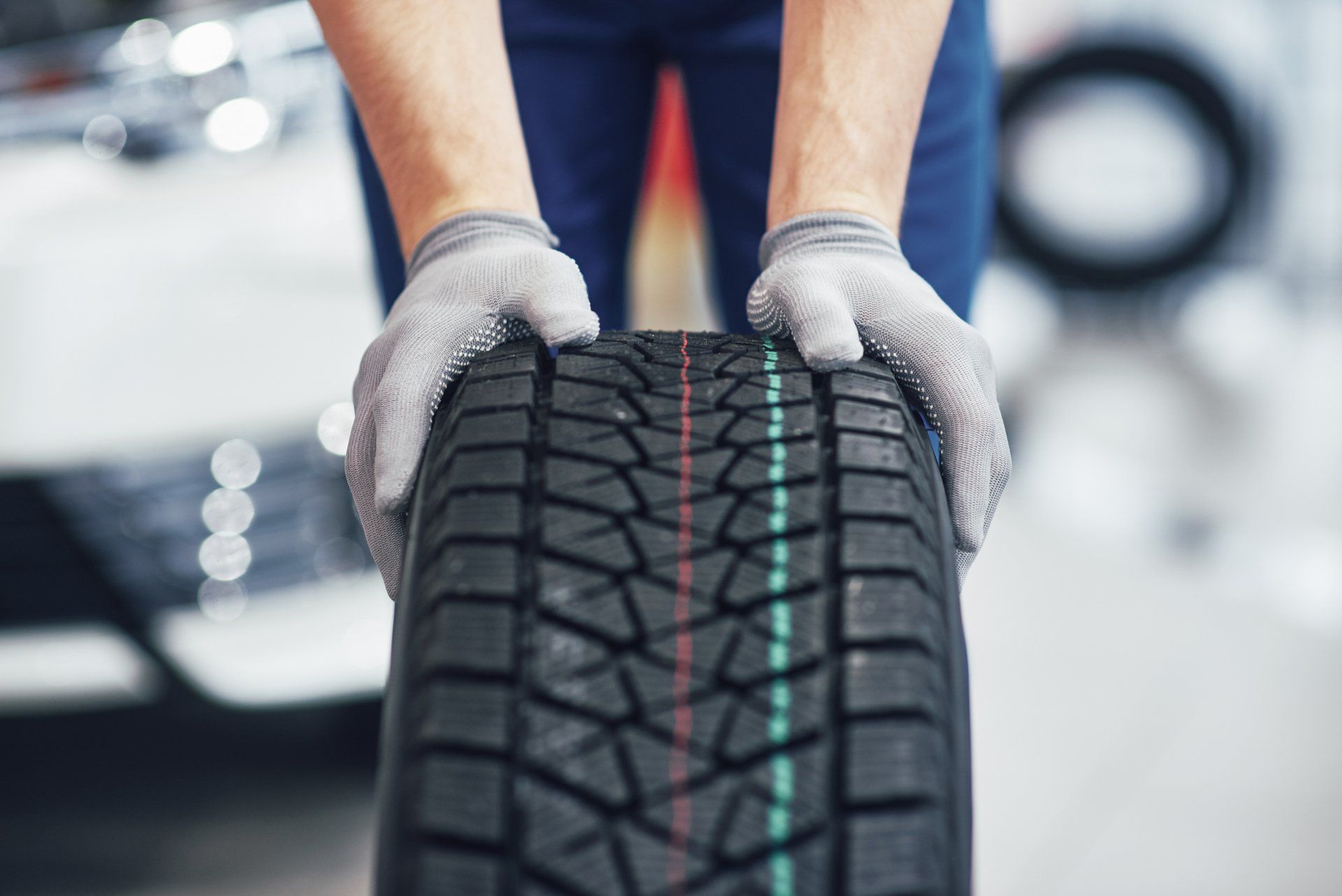 Closeup of mechanic hands pushing a black tire in the workshop.