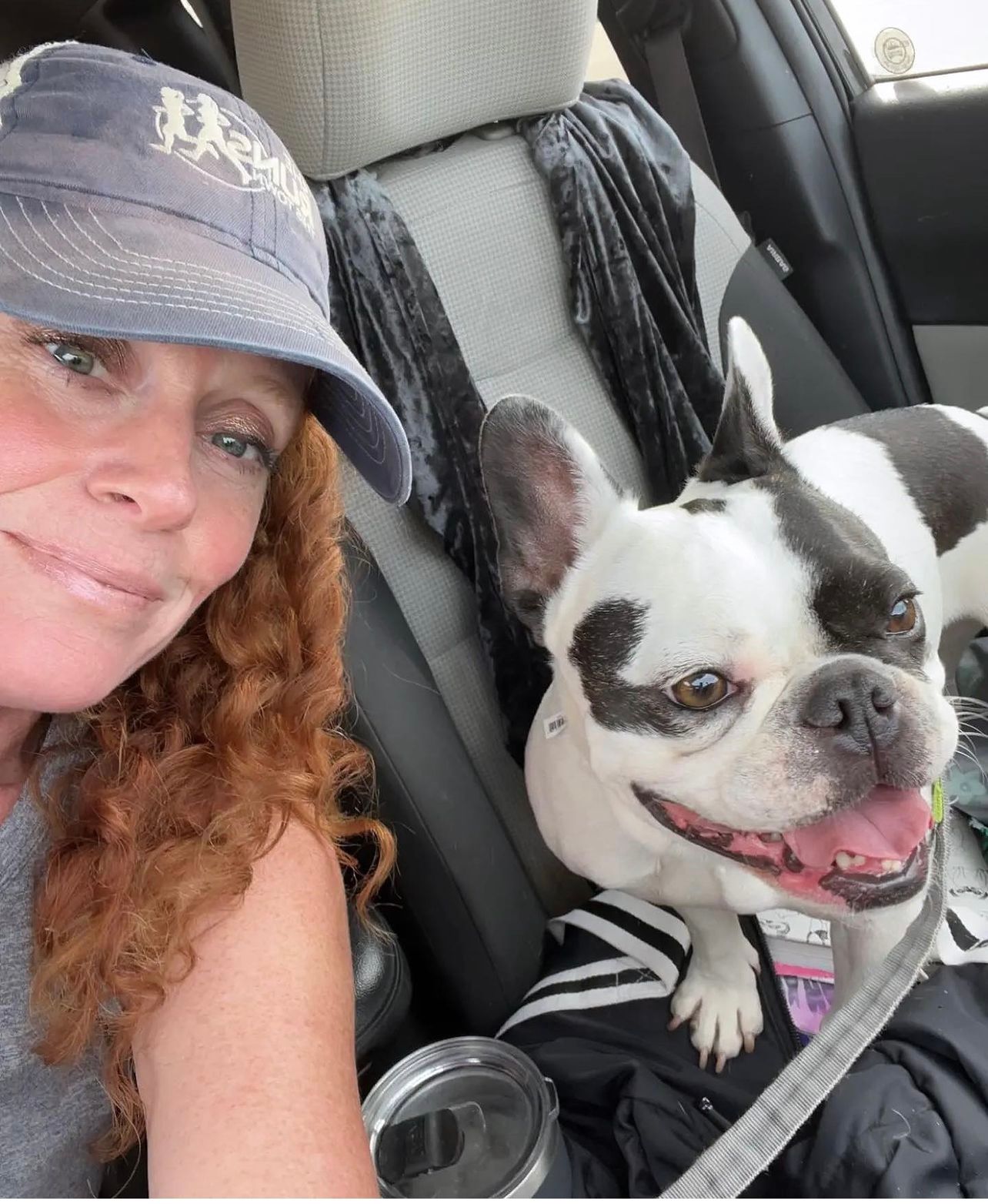 A woman is sitting in the back seat of a car next to a black and white dog.