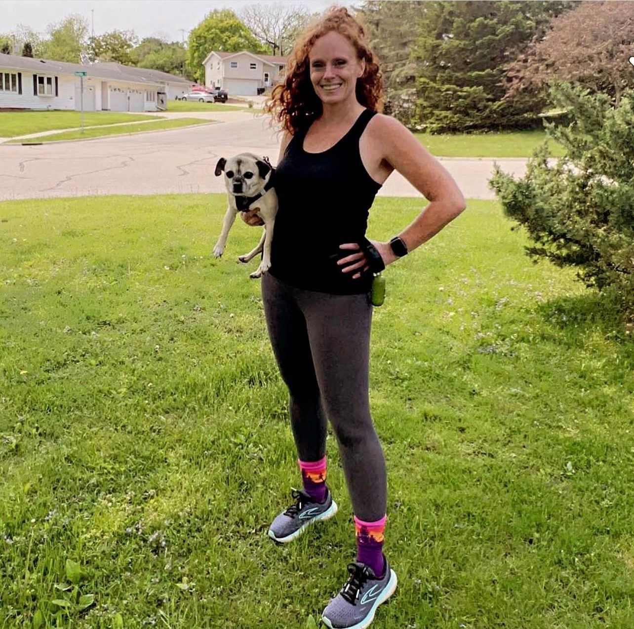 A woman is standing in the grass holding a small dog
