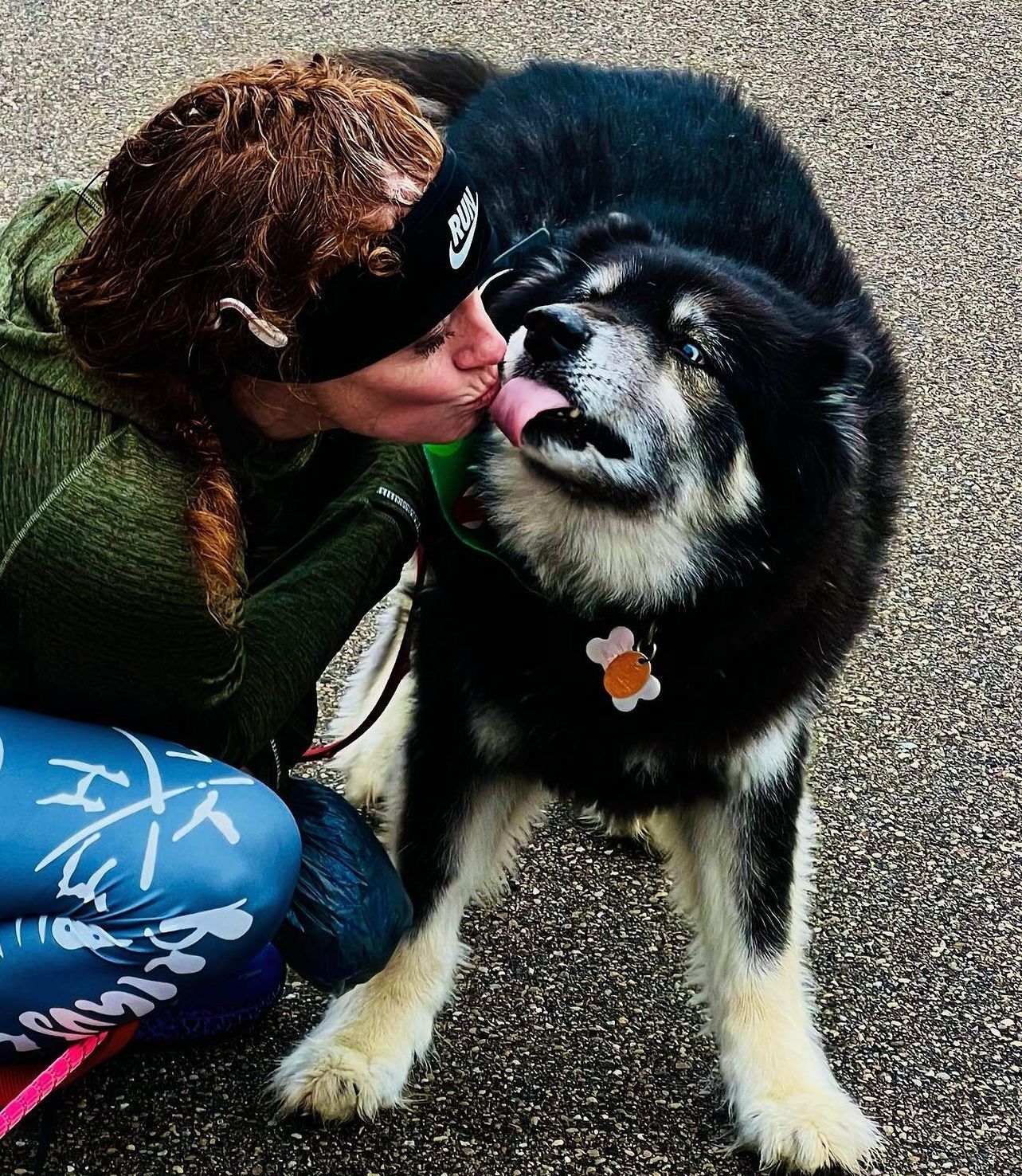 A woman kisses a dog on the cheek while wearing a nike headband