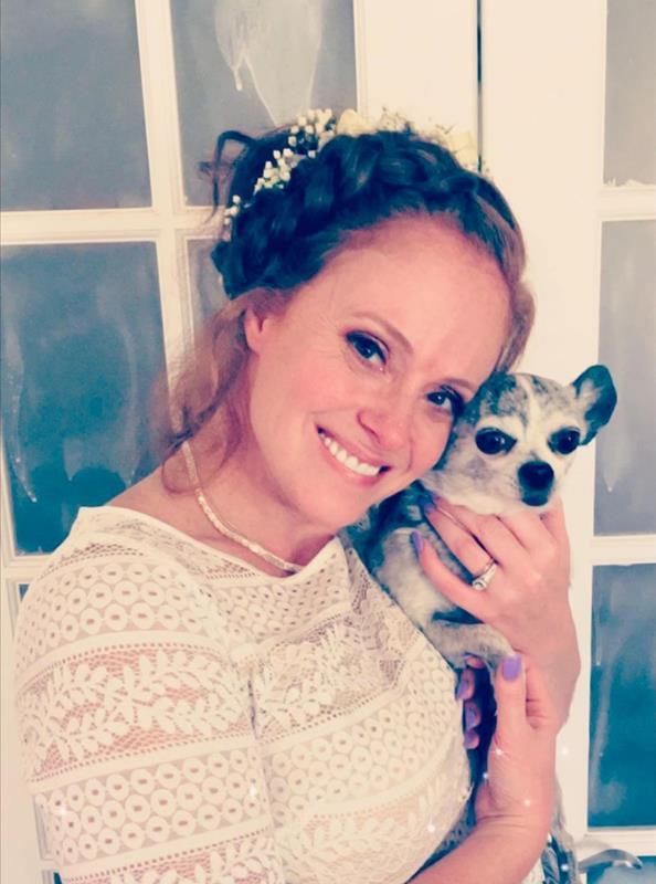 A woman in a white dress is holding a small dog