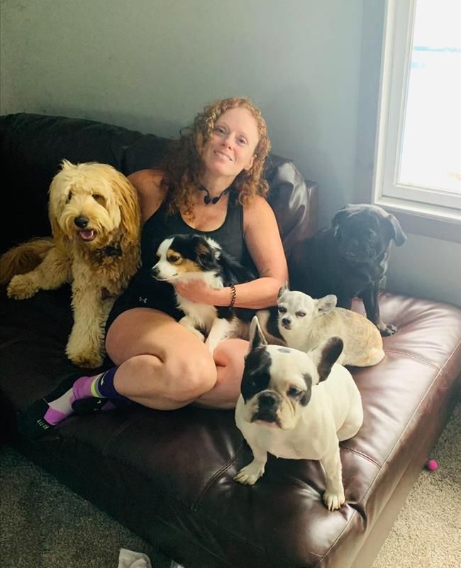 A woman is sitting on a couch surrounded by dogs.