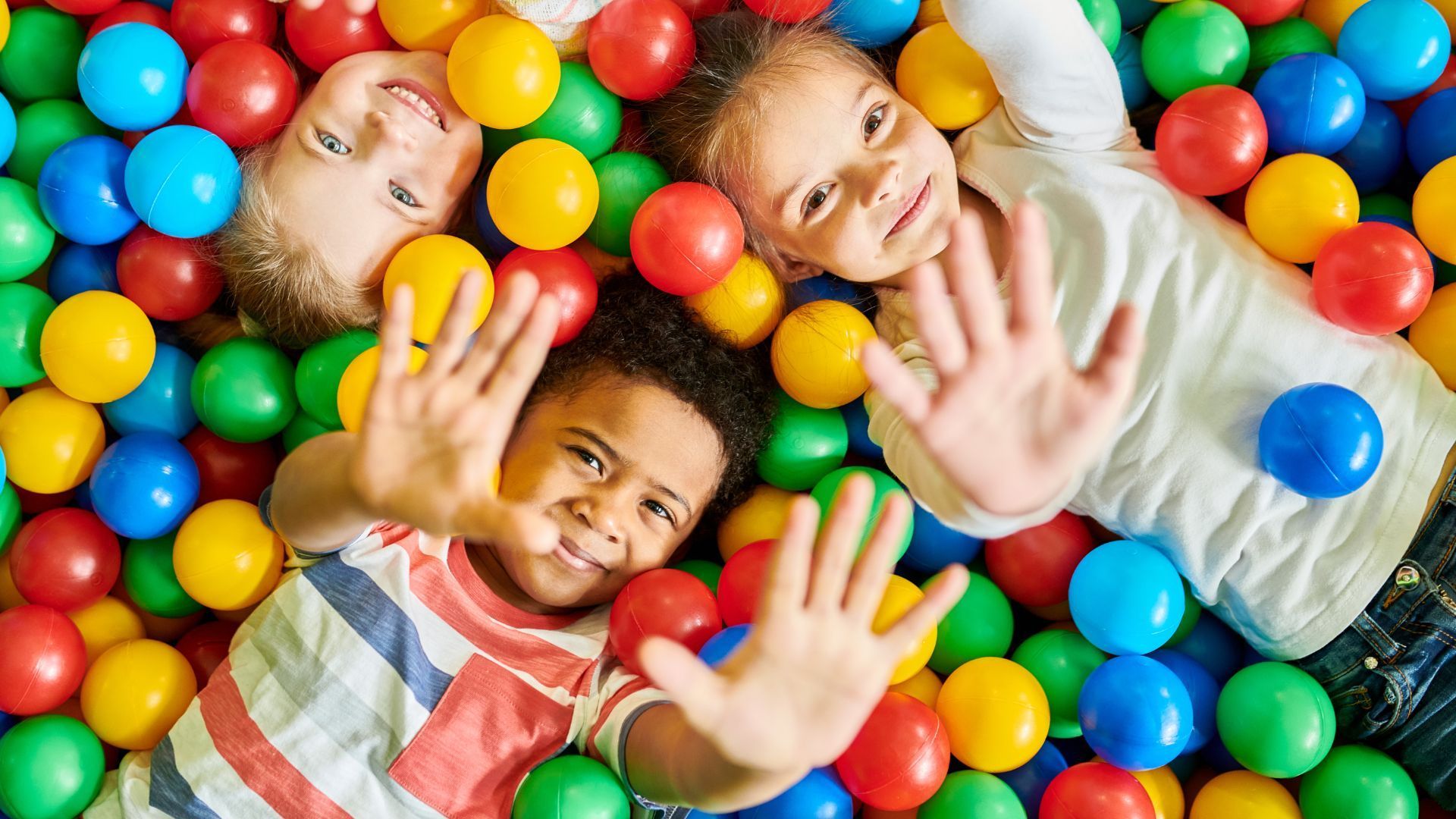 Three children are laying in a ball pit.