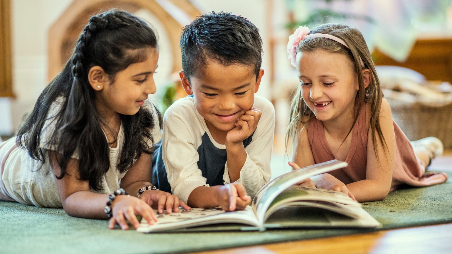Three children are laying on the floor reading a book together.