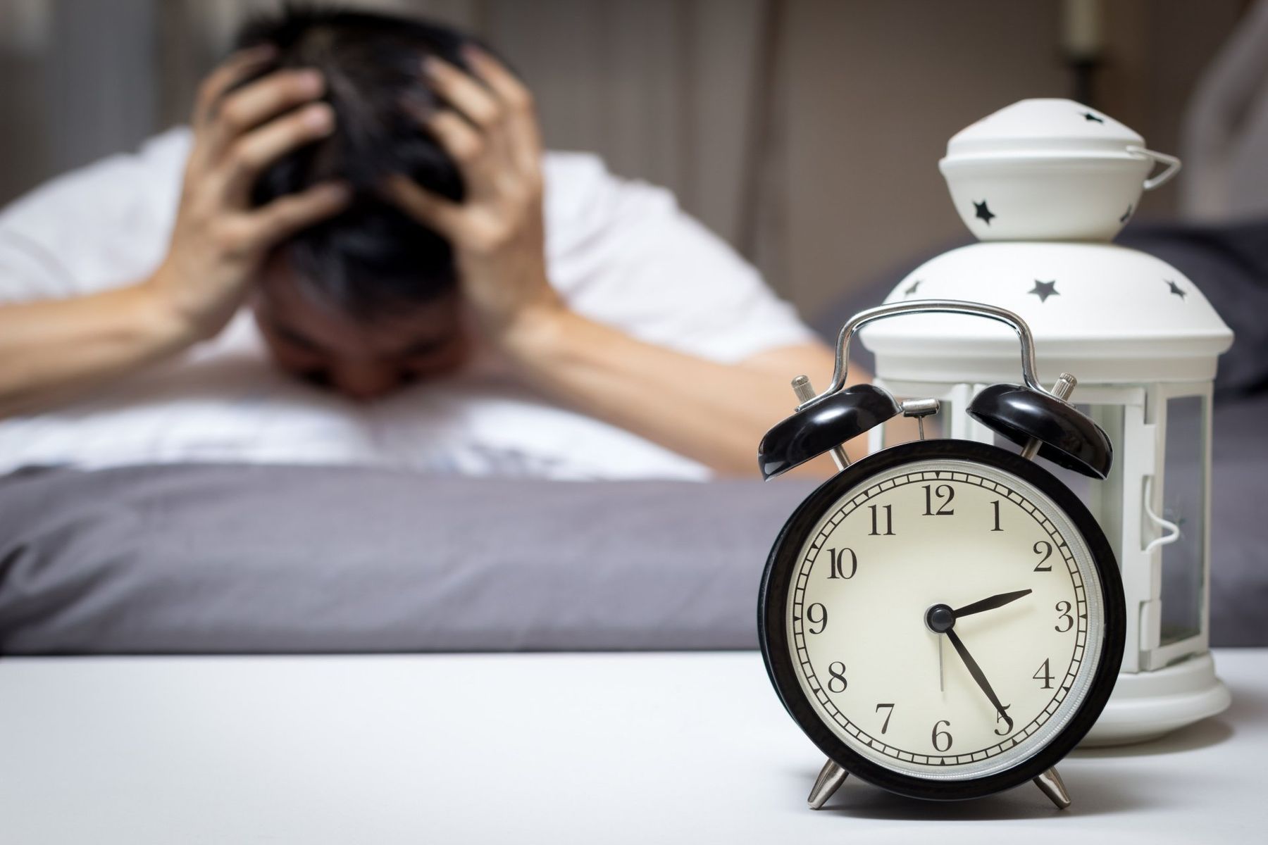 A Man is Laying in Bed Next to an Alarm Clock — Mid North Coast Sleep Clinic in Taree, NSW