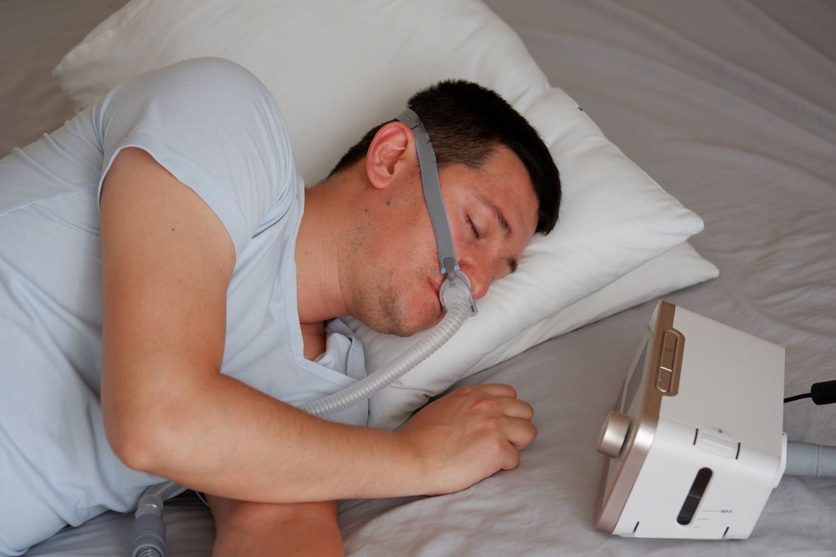 A Man is Sleeping on a Bed With an Oxygen Mask on His Face — Mid North Coast Sleep Clinic in Forster, NSW