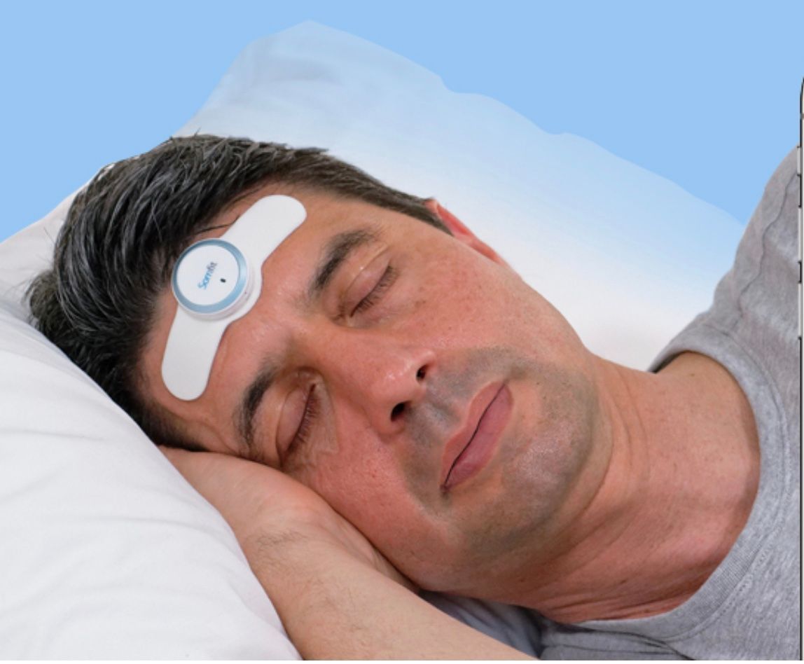 A Man is Laying in Bed With a Device on His Forehead — Mid North Coast Sleep Clinic in Forster, NSW