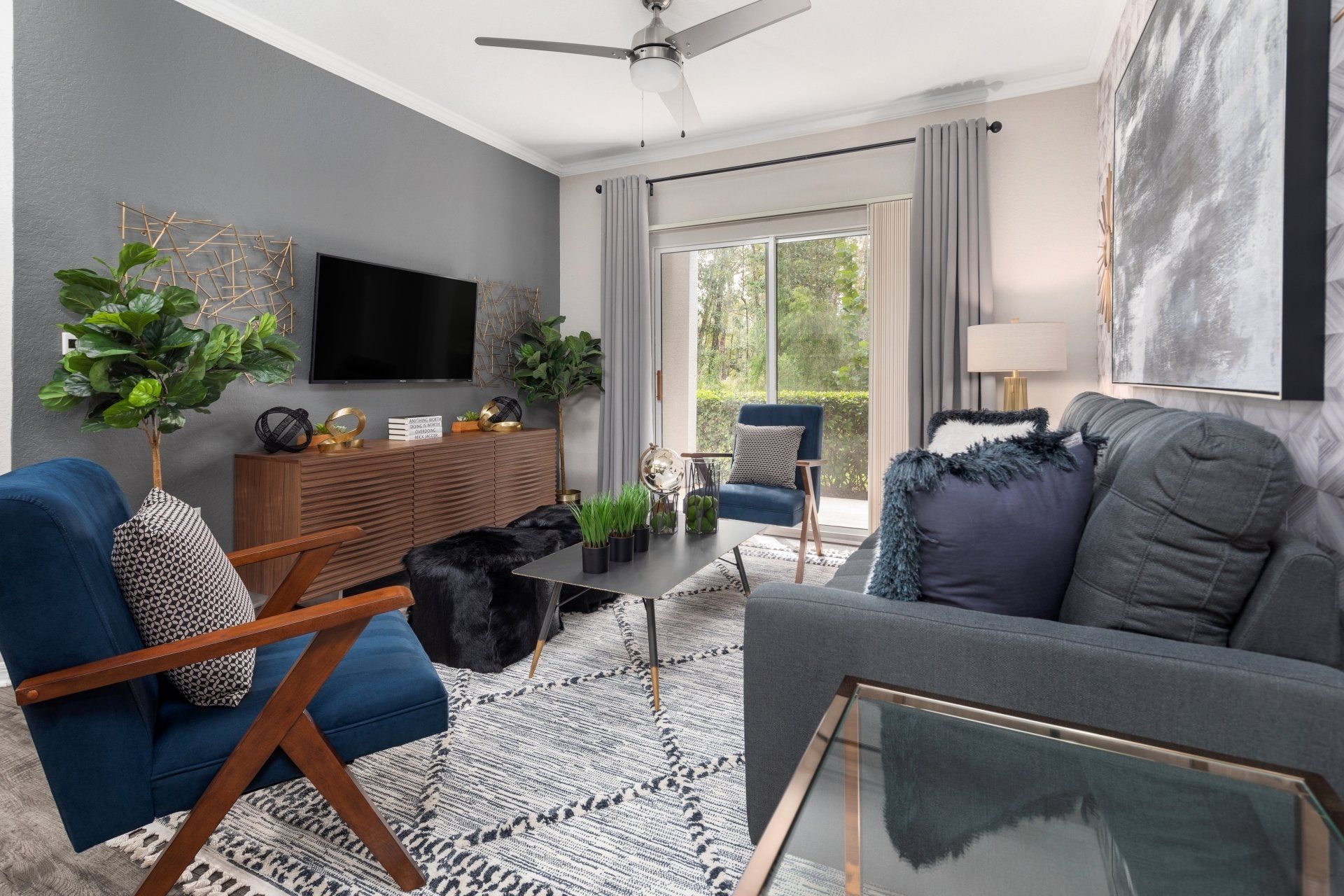 A living room with a couch , chairs , a television and a ceiling fan.