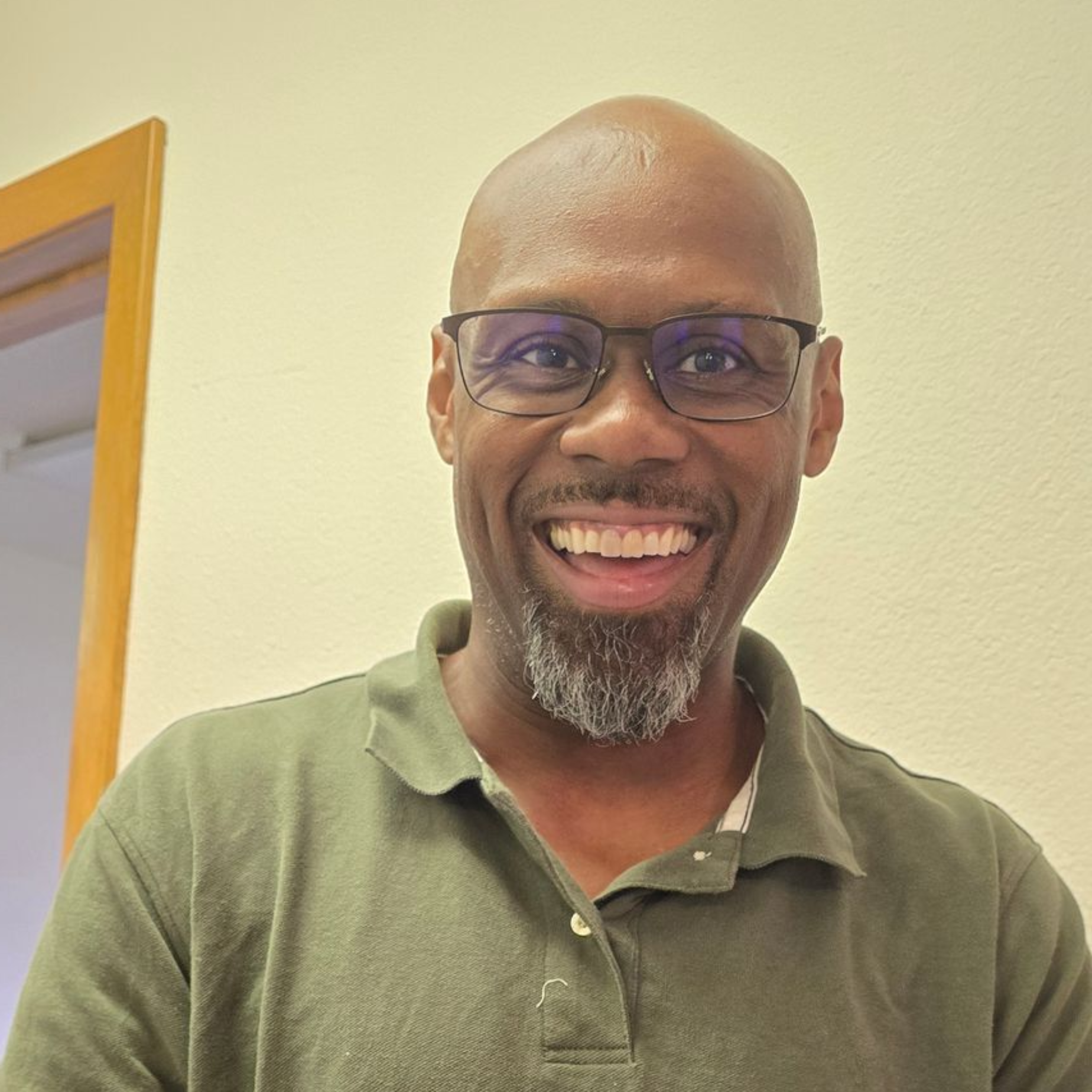 Smiling Black man with glasses and goatee wearing a green polo shirt.