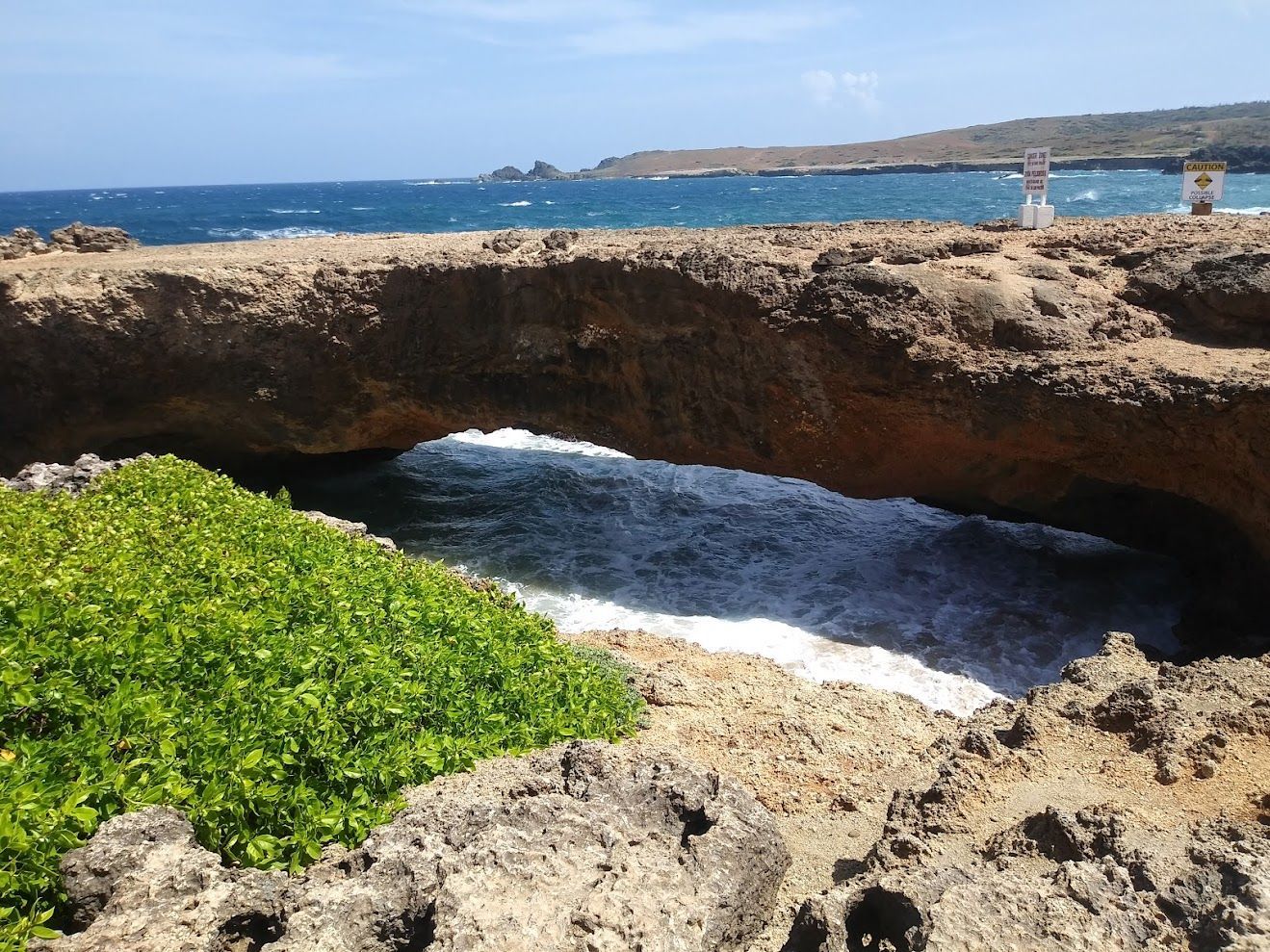 A natural stone bridge arching over turquoise ocean waves against a rocky coastline.
