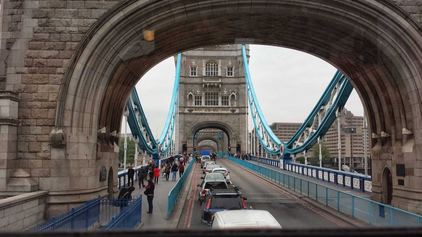 A view from inside the stone arch of Tower Bridge in London, looking down a road with cars and pedestrians.