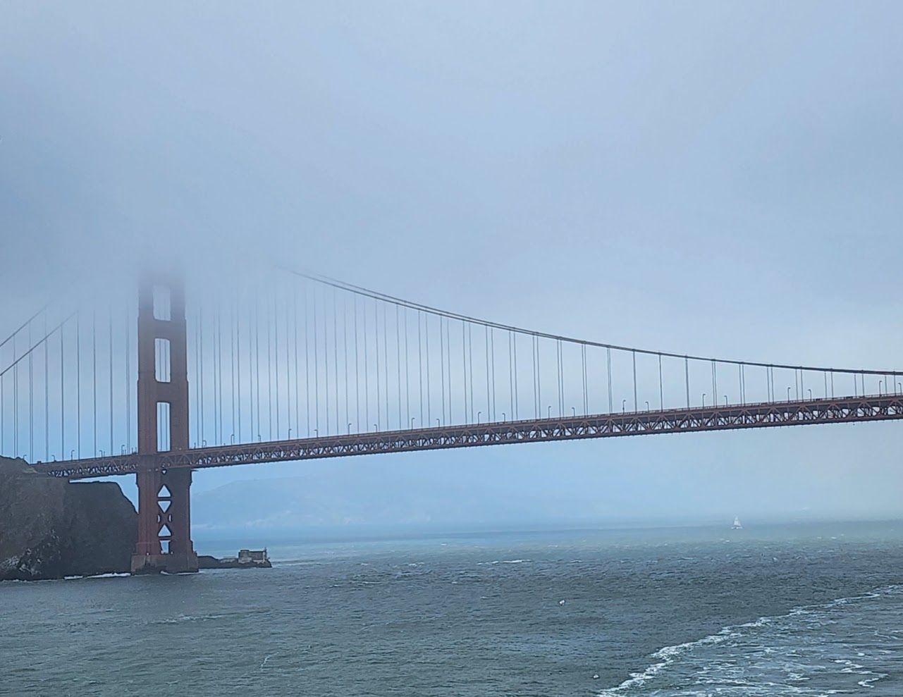 The Golden Gate Bridge rises out of the water against a foggy, overcast sky.