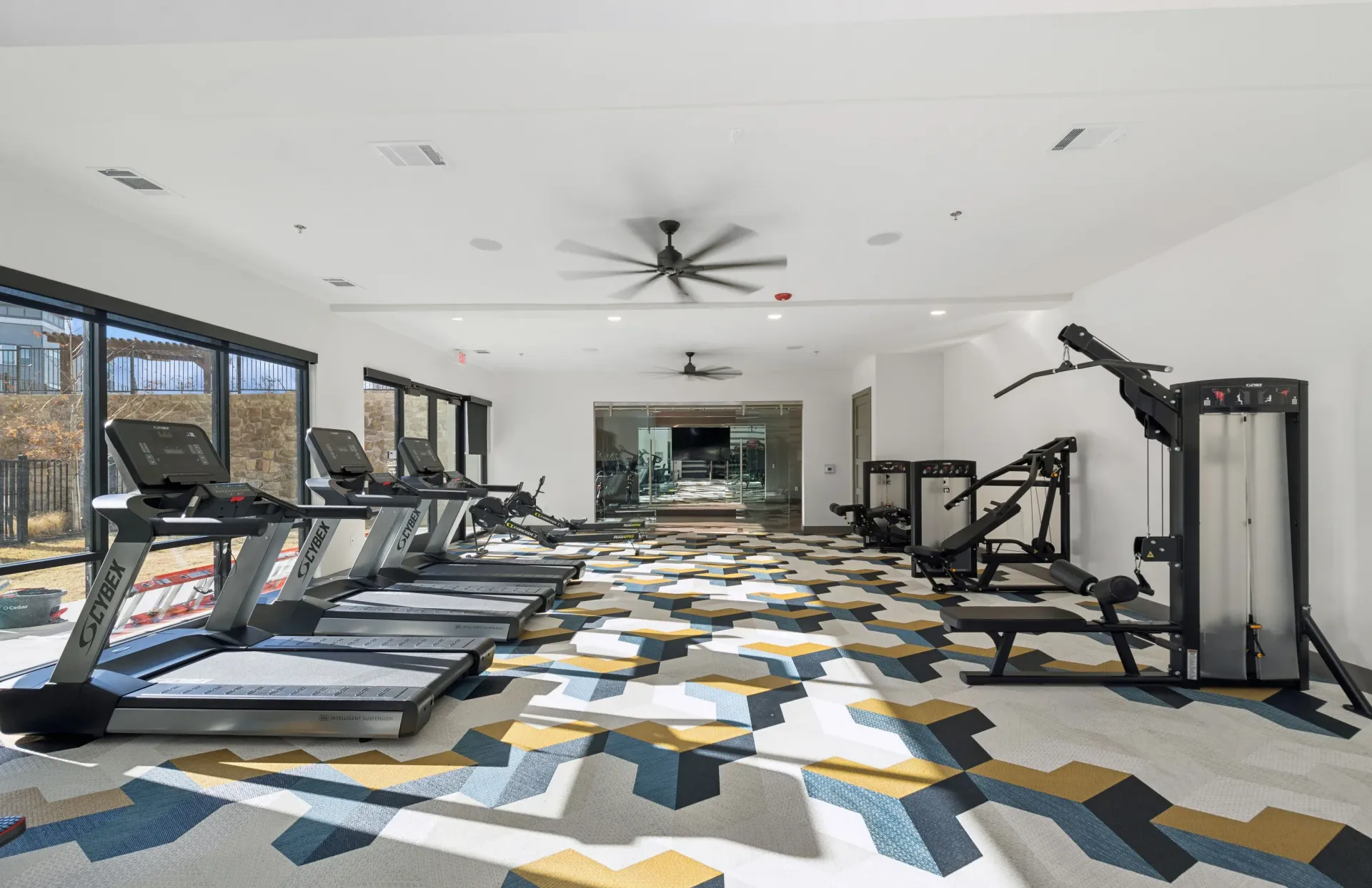 Bright fitness center with treadmills and weight machines along a windowed wall.