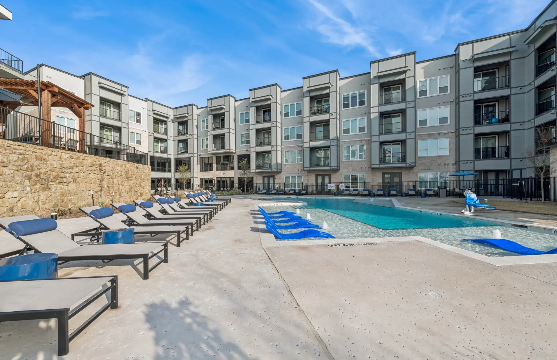 Outdoor pool area with blue lounge chairs and surrounding apartment buildings.