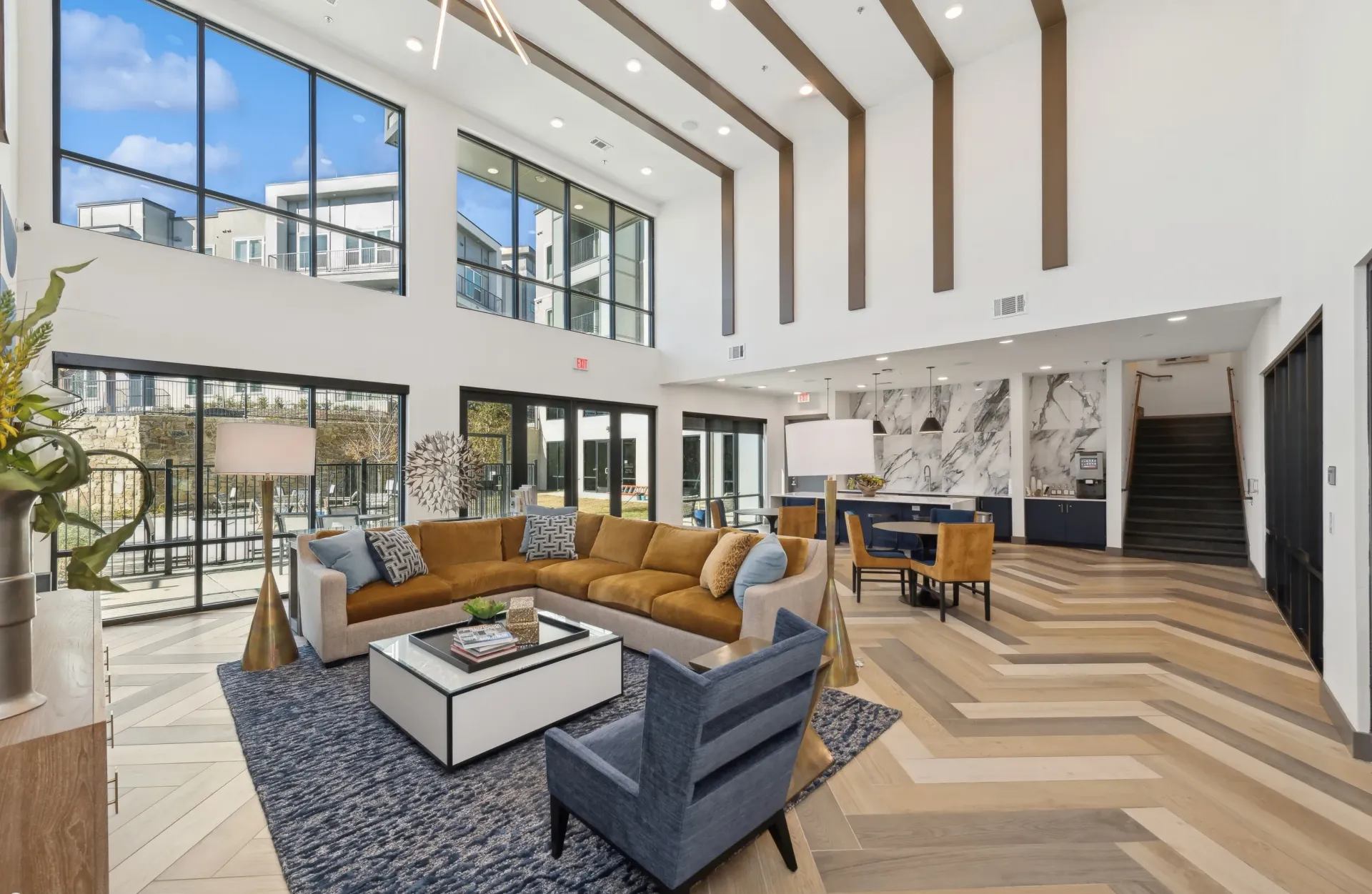 Bright modern apartment lobby with tall windows, high ceilings, and a tan sectional sofa.