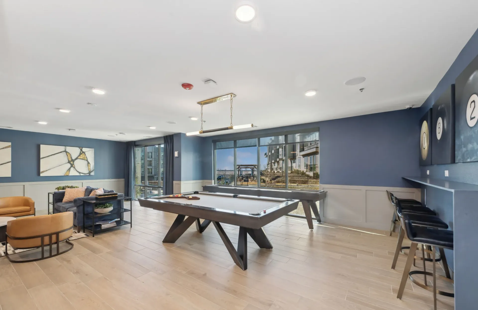 Indoor community recreation room with a pool table, lounge seating, and large windows.