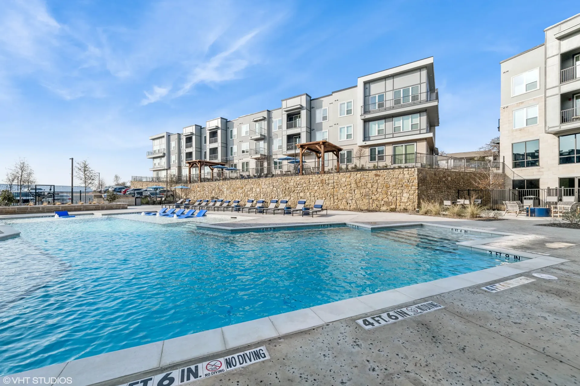Outdoor pool area of a multifamily community with lounge chairs and a stone retaining wall.