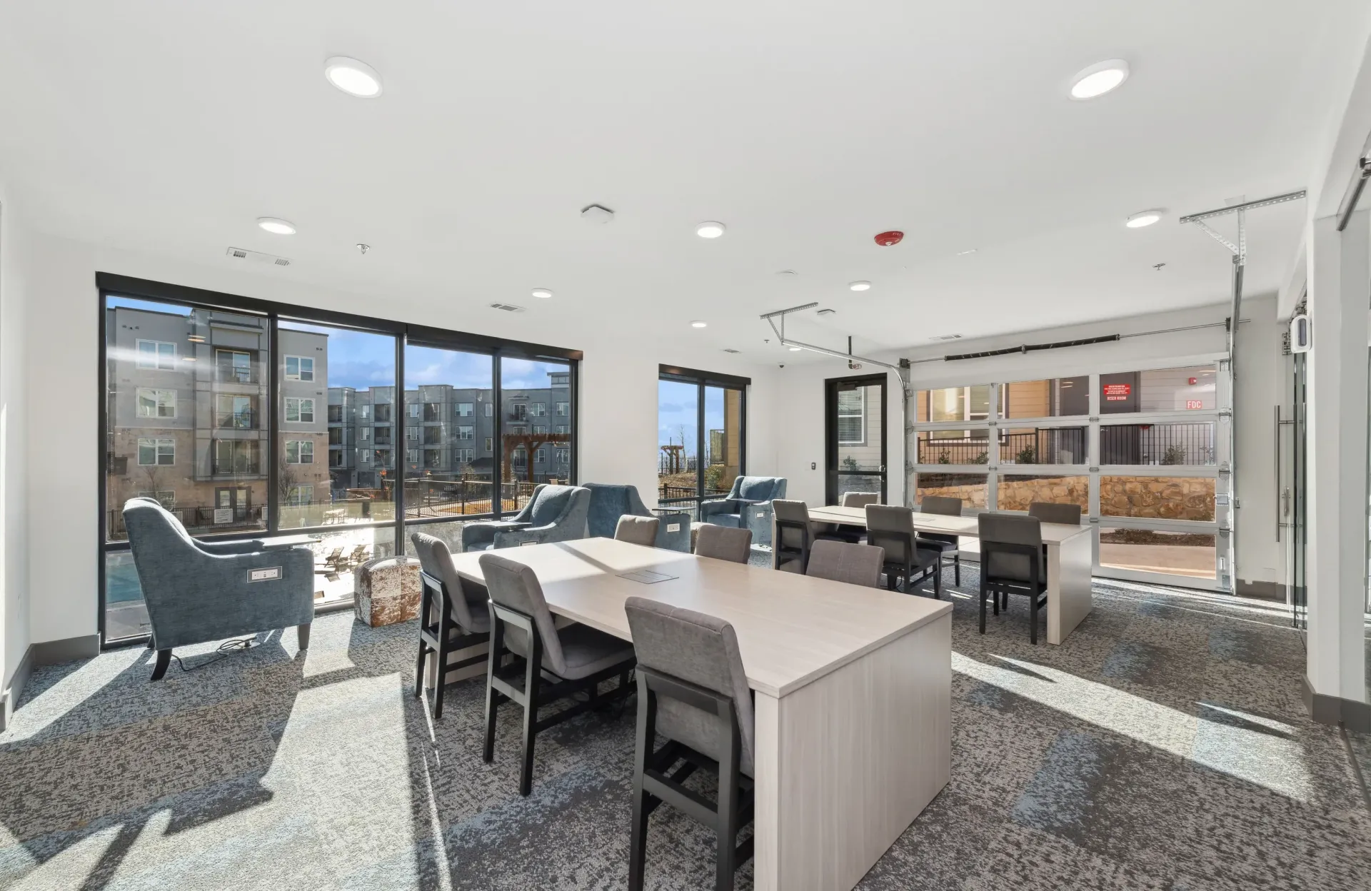 Bright community lounge with large windows, seating areas and tables.