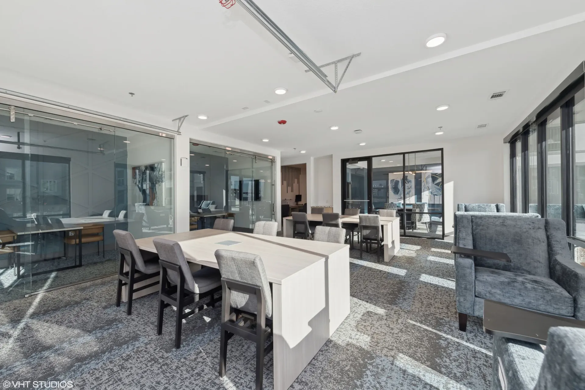 Modern apartment community lounge with glass walls, multiple seating areas and tables.