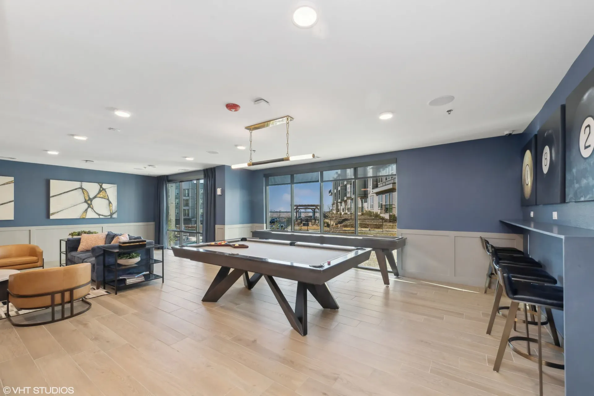 Indoor community recreation room with pool table, lounge seating, and large windows.