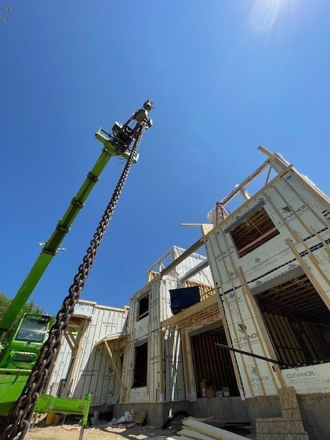 Une grue verte est attachée à une chaîne devant une maison en construction.
