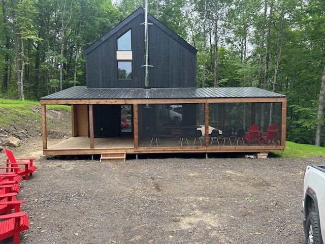 Une maison noire avec un porche grillagé dans les bois