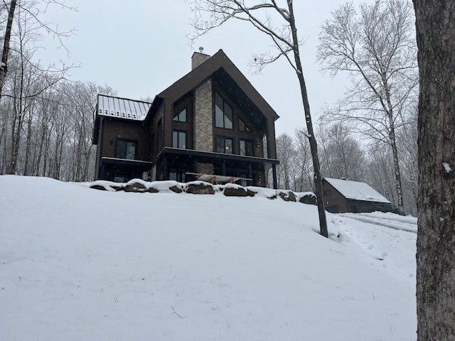 Une grande maison est assise au sommet d'une colline couverte de neige entourée d'arbres.