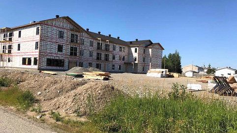 Un grand bâtiment est en construction dans un champ à côté d'une route.