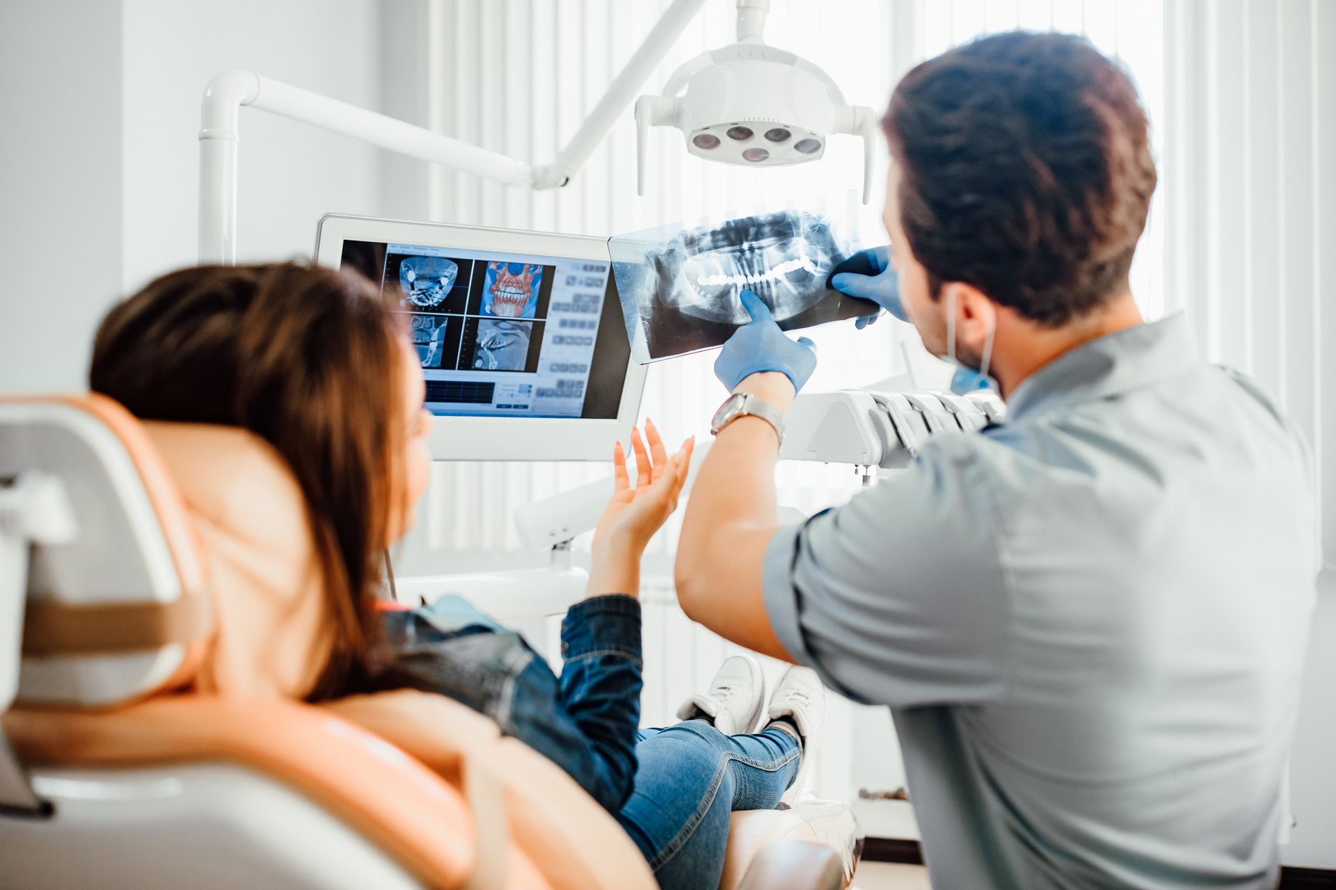 A dentist is showing a dental X-ray to a female patient at the dental clinic office.