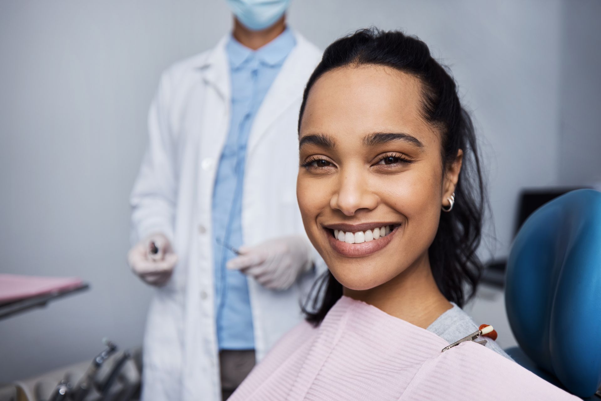 A smiling woman in a dental office with a dentist behind her