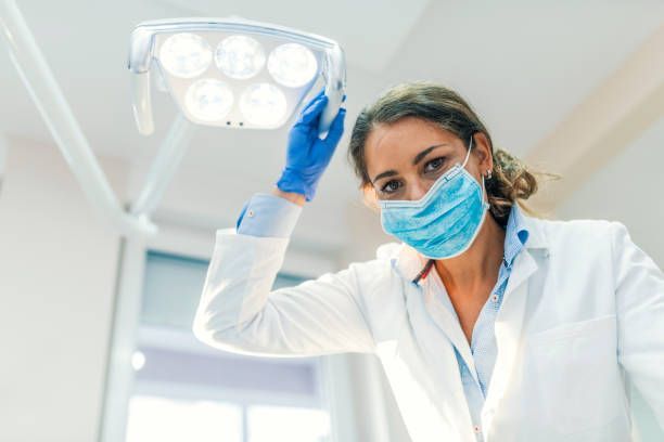 A female dentist wearing a mask and gloves is holding a light.