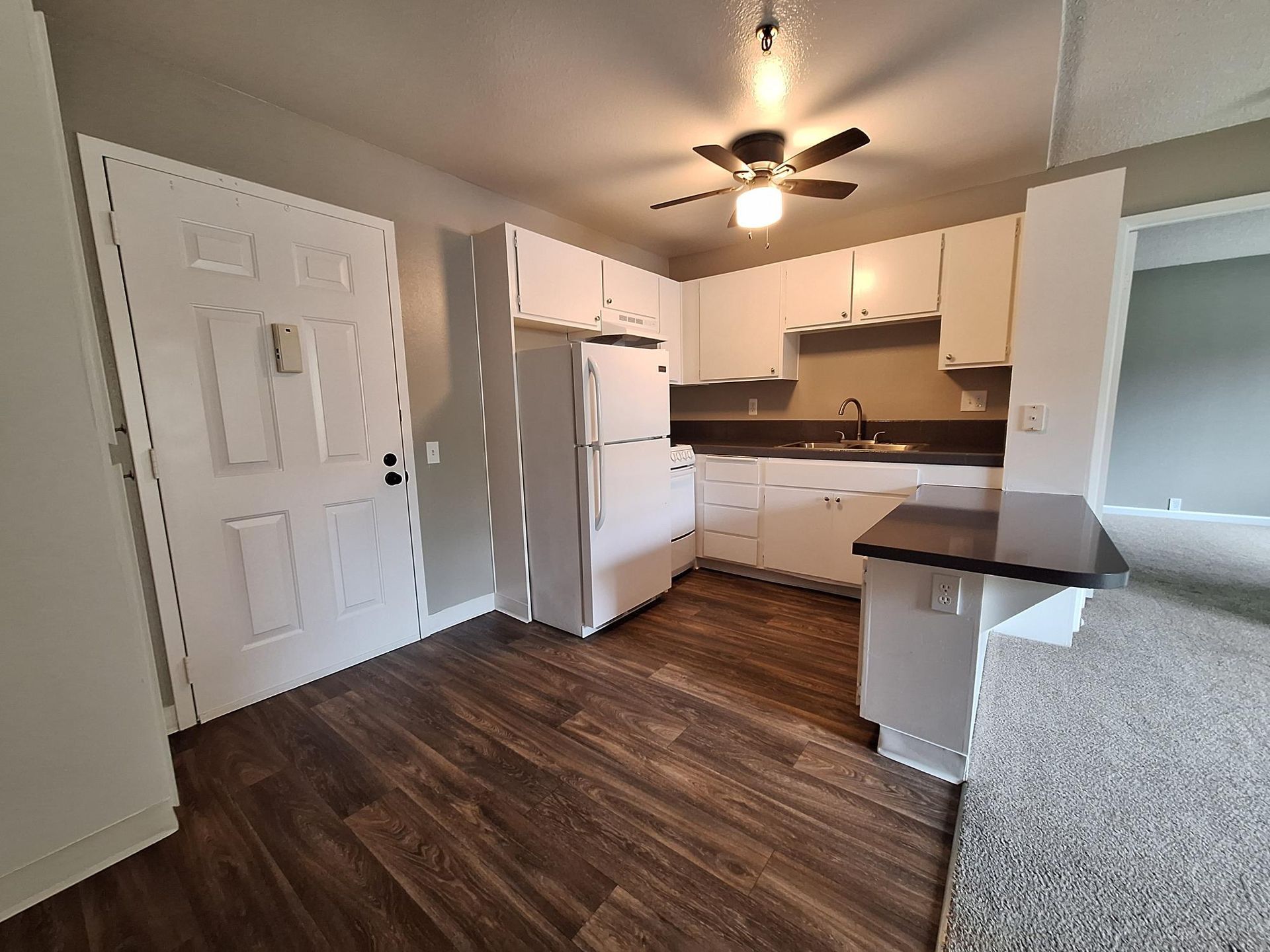A kitchen with white cabinets , a refrigerator , a sink , and a ceiling fan.